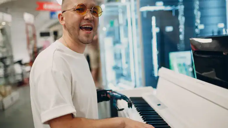 A Person Wearing Shades And Playing A Piano. The Person Has A Prosthetic Arm.
