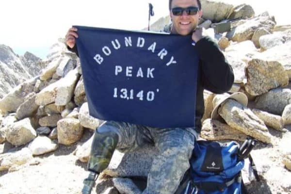 A Person Sitting At A Rocky Area Wearing Shades. The Person Is Holding A Flag.