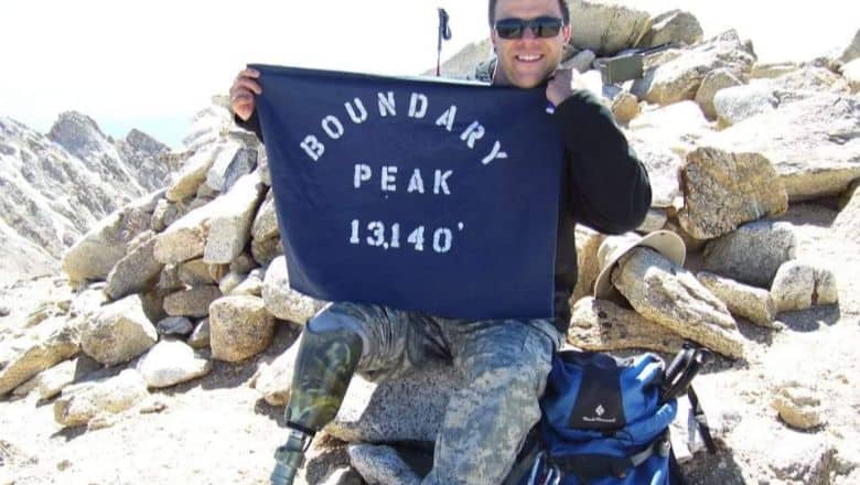 A Person Sitting At A Rocky Area Wearing Shades. The Person Is Holding A Flag.