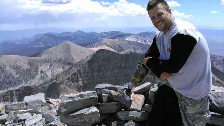 Military Veteran With Prosthetic Perched On The Side Of A Mountain